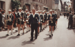 Jugendkapelle in Uniform mit kurzen Hosen und weißer Mütze bei einem Festzug unter Leitung von Anton Hartmann